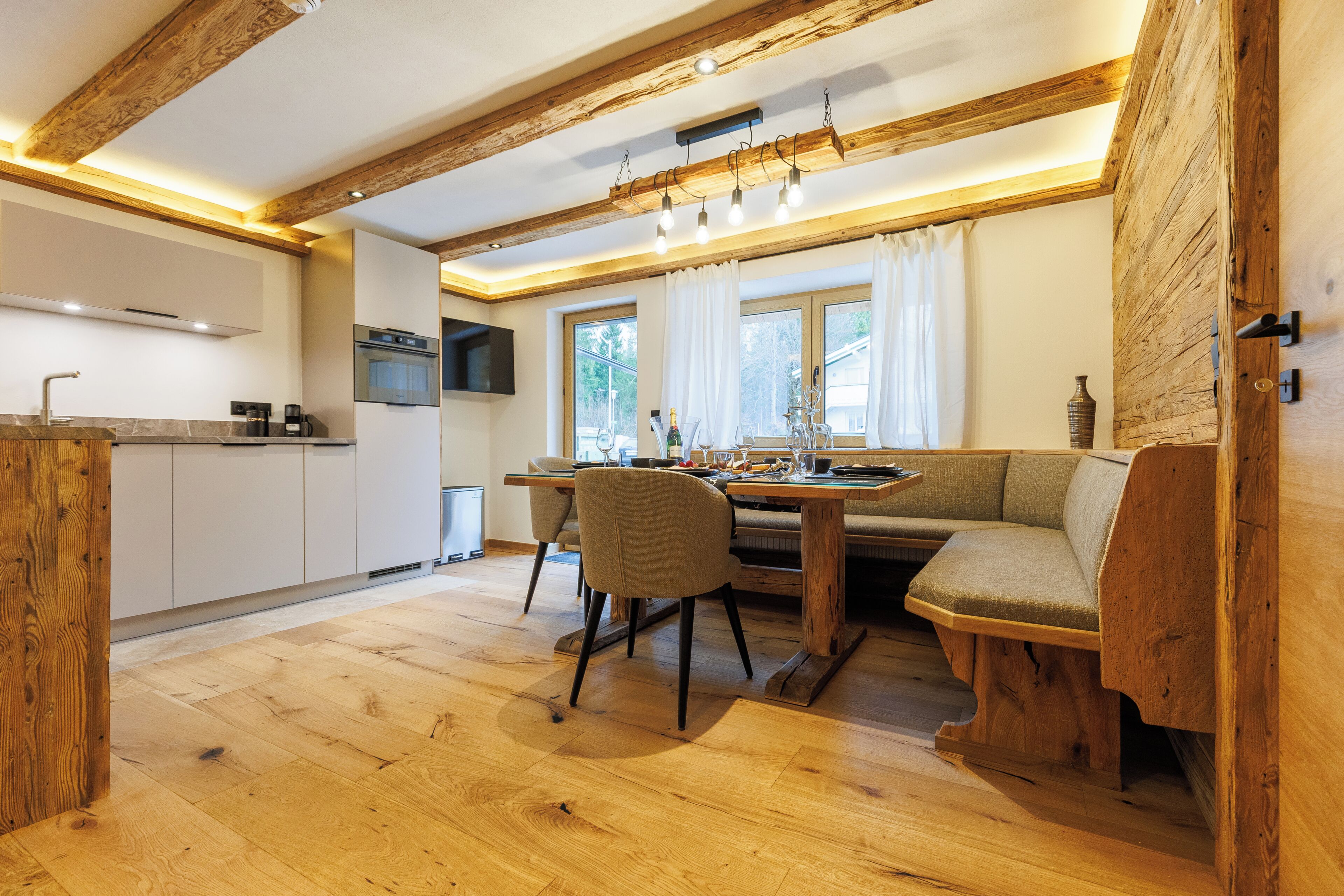 Una cocina moderna con vigas de madera, un comedor con una mesa y sillas de madera, y un horno empotrado.