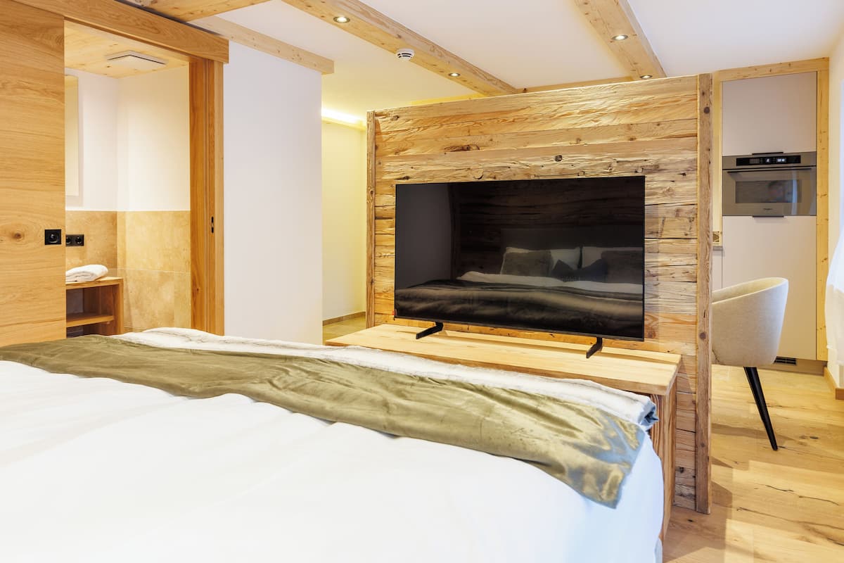 Um quarto moderno com uma cama grande, televisão integrada e uma parede de destaque em madeira.