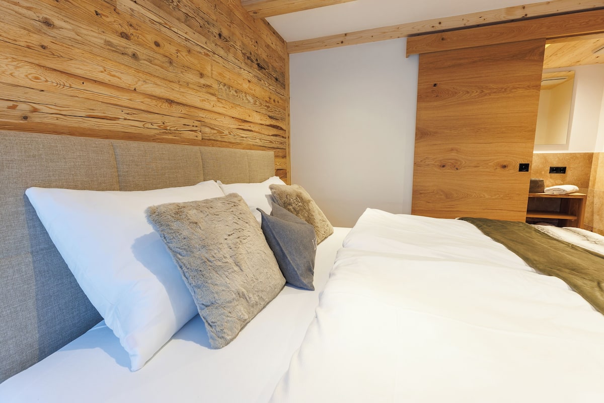 A bedroom with a wooden headboard, a bed with white bedding, and a wooden wardrobe.