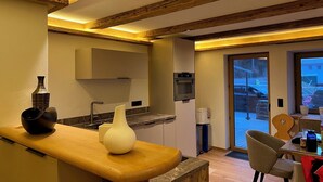 A modern kitchen with wooden beams, a built-in oven, and a dining area with a table and chairs. - Die Steinberg Chalets (St. Ulrich Am Pillersee)