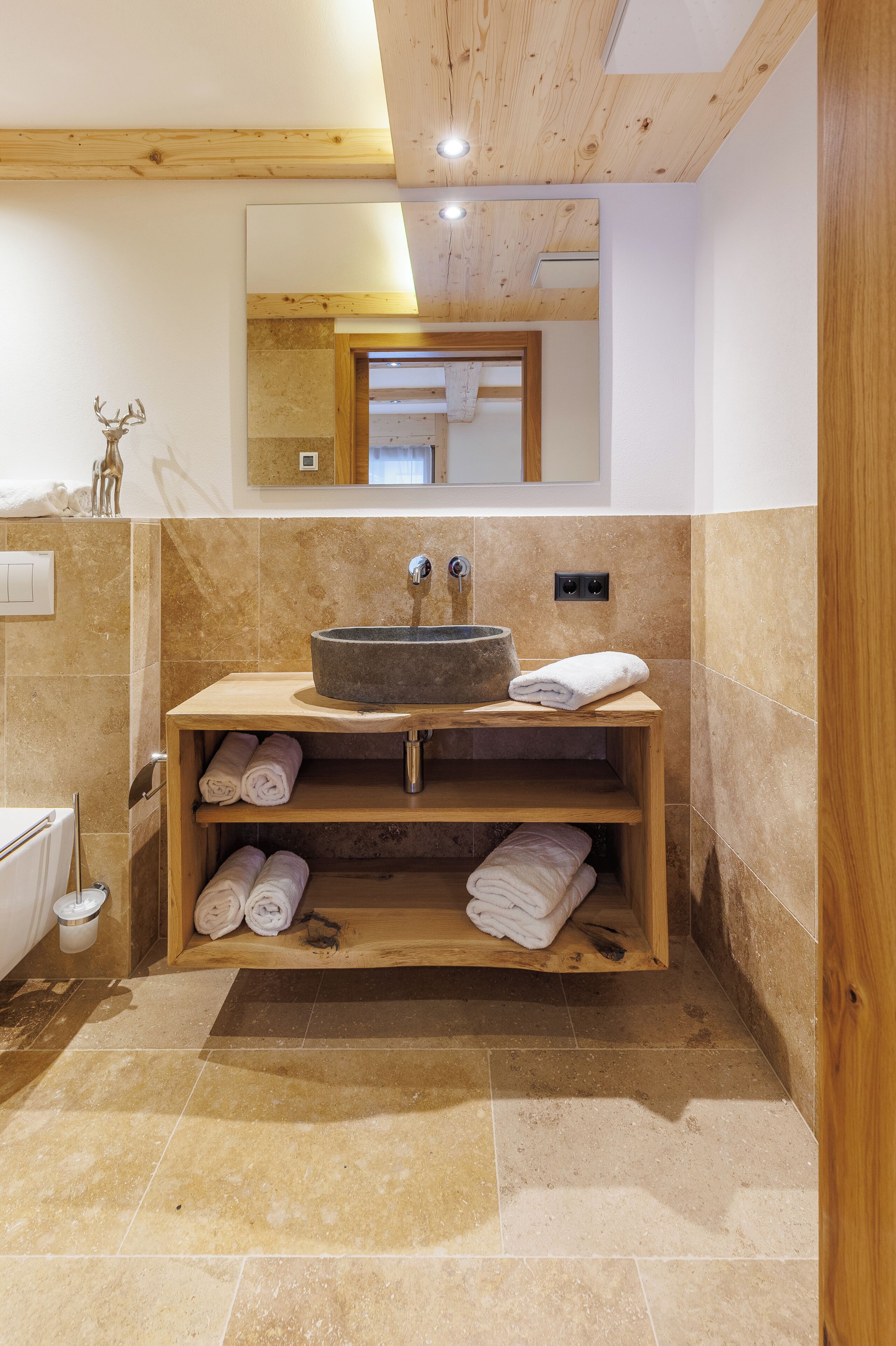 Une salle de bain avec un lavabo en pierre, des étagères en bois et un miroir au-dessus du lavabo.