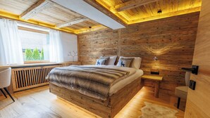 A bedroom with a wooden bed, a window with curtains, a desk, and a chair. - Die Steinberg Chalets (St. Ulrich Am Pillersee)