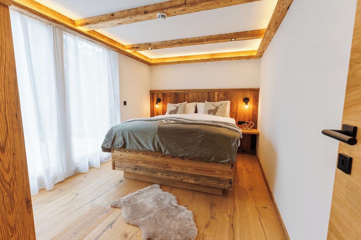 Quarto com cama de madeira, tapete de pele e mesa de cabeceira com abajur.