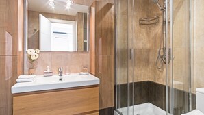 Een moderne badkamer met een douchecabine van glas, een houten wastafelmeubel met spiegel en een witte wasbak.