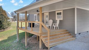 A covered porch with a wooden staircase leading to a seating area with chairs and a table. - Cozy Modern Farmhouse near Normandy Lake (Normandy)