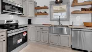 A modern kitchen with stainless steel appliances, white cabinetry, and wooden shelves. - Cozy Modern Farmhouse near Normandy Lake (Normandy)
