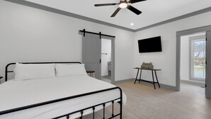 A bedroom with a bed, a ceiling fan, a mounted TV, and a small table with a model house. - Cozy Modern Farmhouse near Normandy Lake (Normandy)