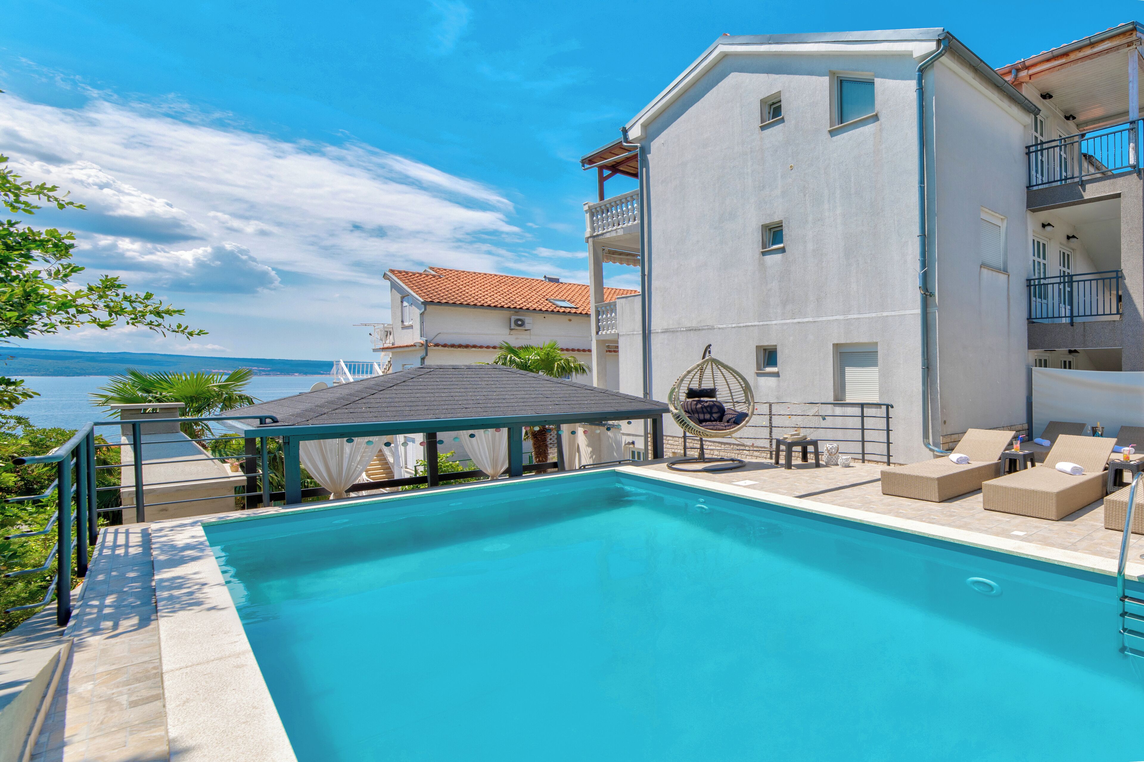 Ein Pool mit Liegestühlen und einer überdachten Sitzecke mit Blick auf ein Gewässer.
