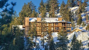Een lodge met meerdere verdiepingen, omgeven door met sneeuw bedekte bergen en dichte dennenbomen.