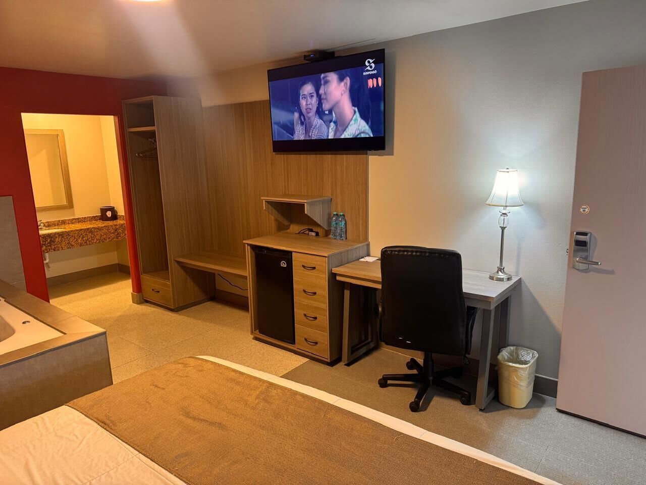 A hotel room with a bed, a desk, a chair, a TV, a wardrobe, and a bathroom.