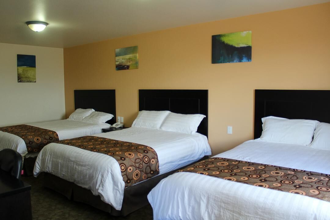 A hotel room with three beds, each with a headboard, a bedside table, and a lamp.