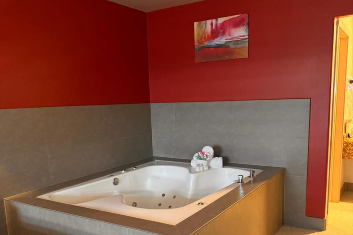 A modern bathroom with a large bathtub, red walls, and a gray headboard.