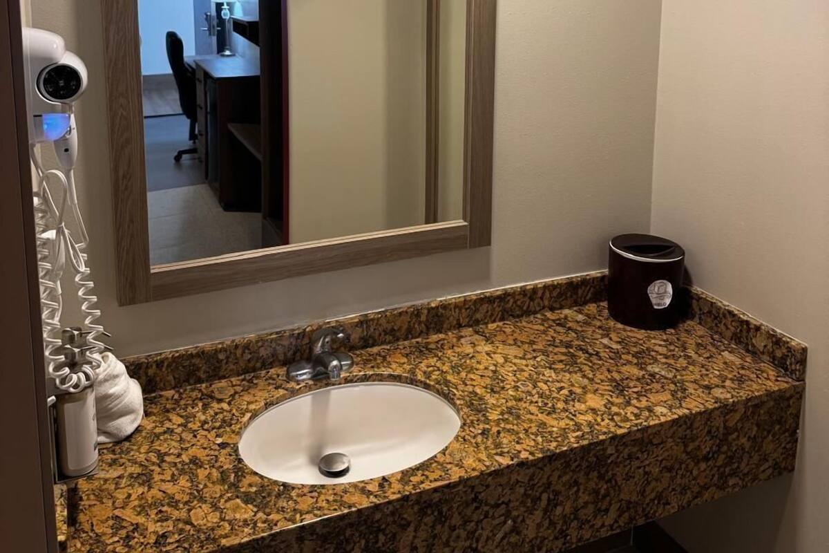 Ein Badezimmer mit Granitwaschtisch, Waschbecken, Spiegel, Fön und Mülleimer.