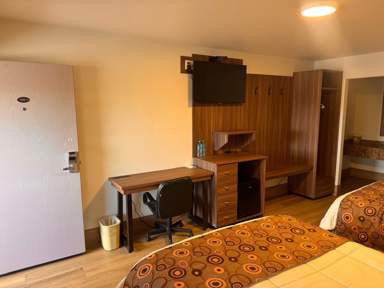 Een hotelkamer met een houten bureau, een televisie, twee bedden met beddengoed met een patroon en een kledingkast.