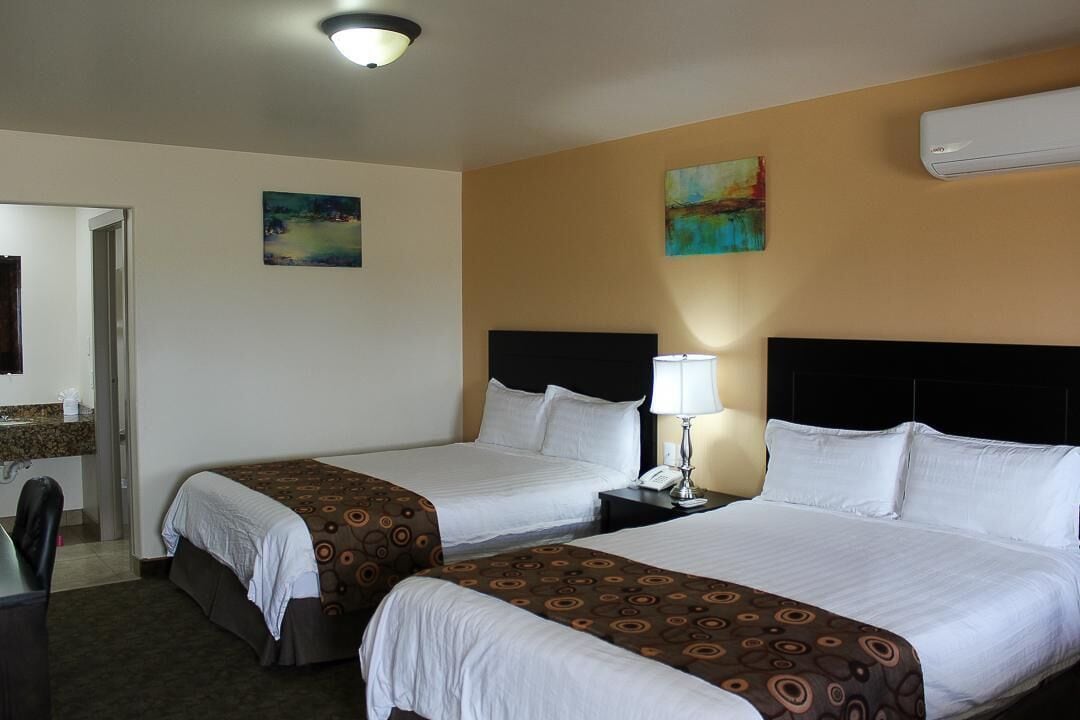Une chambre d’hôtel avec deux lits, un bureau, une chaise, une table de chevet avec une lampe et des œuvres d’art accrochées aux murs.