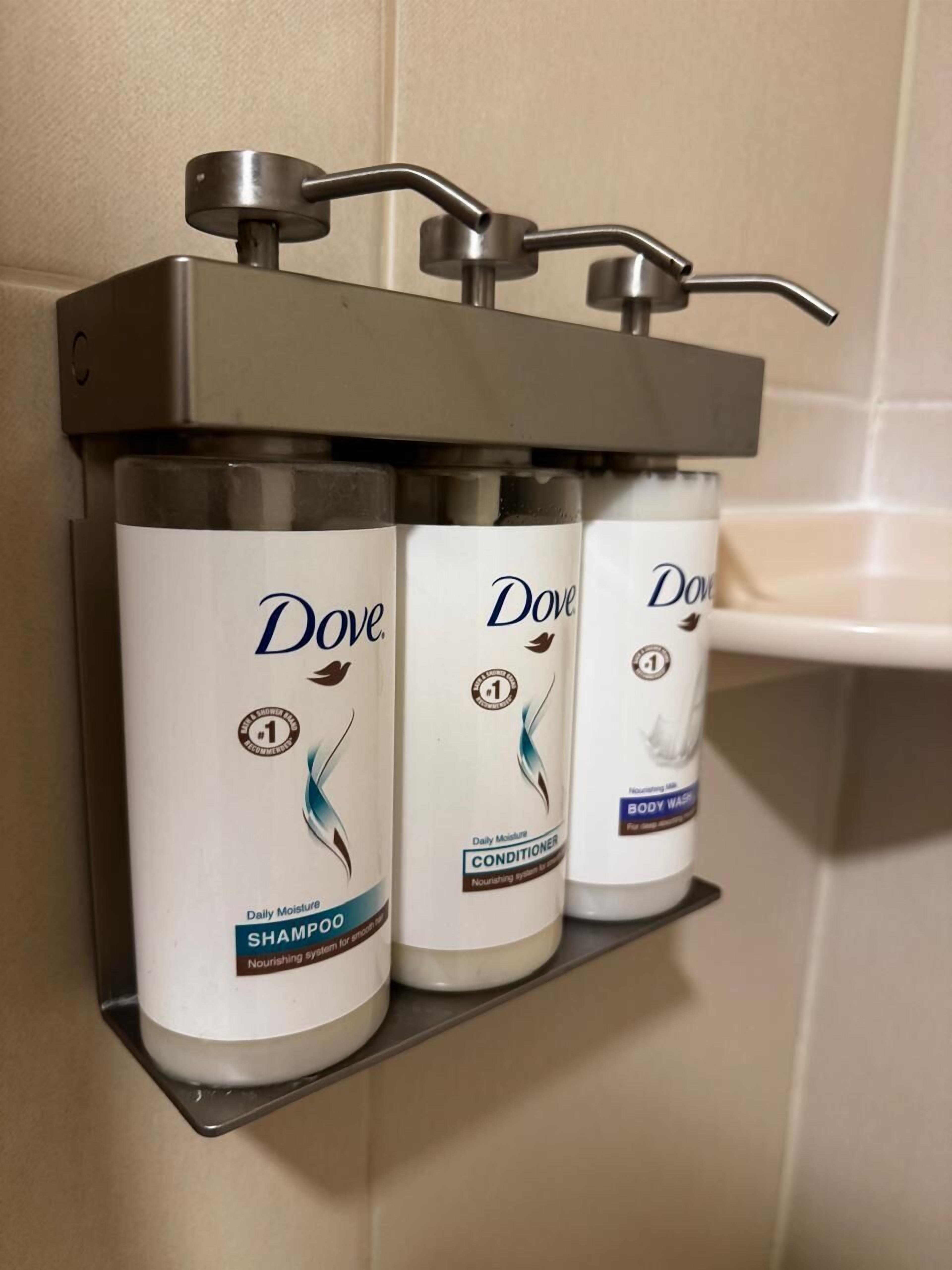 Three Dove personal care products on a metal shelf in a bathroom.