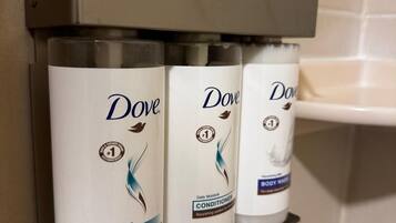 Tres productos de Dove para el cuidado personal sobre una estantería metálica en un baño.