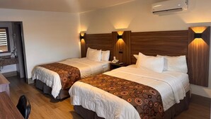 Habitación de hotel con dos camas, un escritorio y un equipo de aire acondicionado.