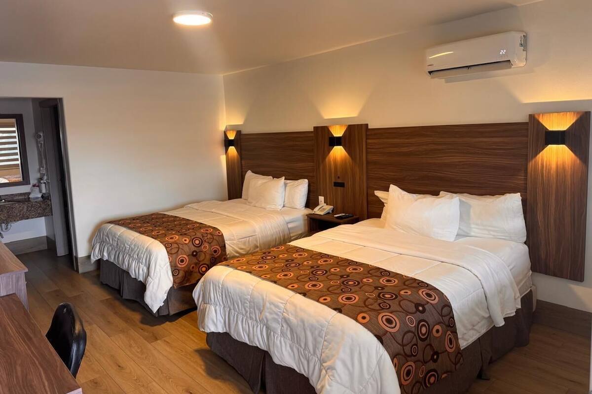 Ein Hotelzimmer mit zwei Betten, einem Schreibtisch und einer Klimaanlage.