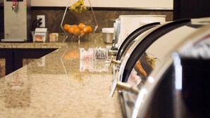 Una encimera de cocina con una cafetera, una cesta de fruta y un recipiente de plástico transparente.