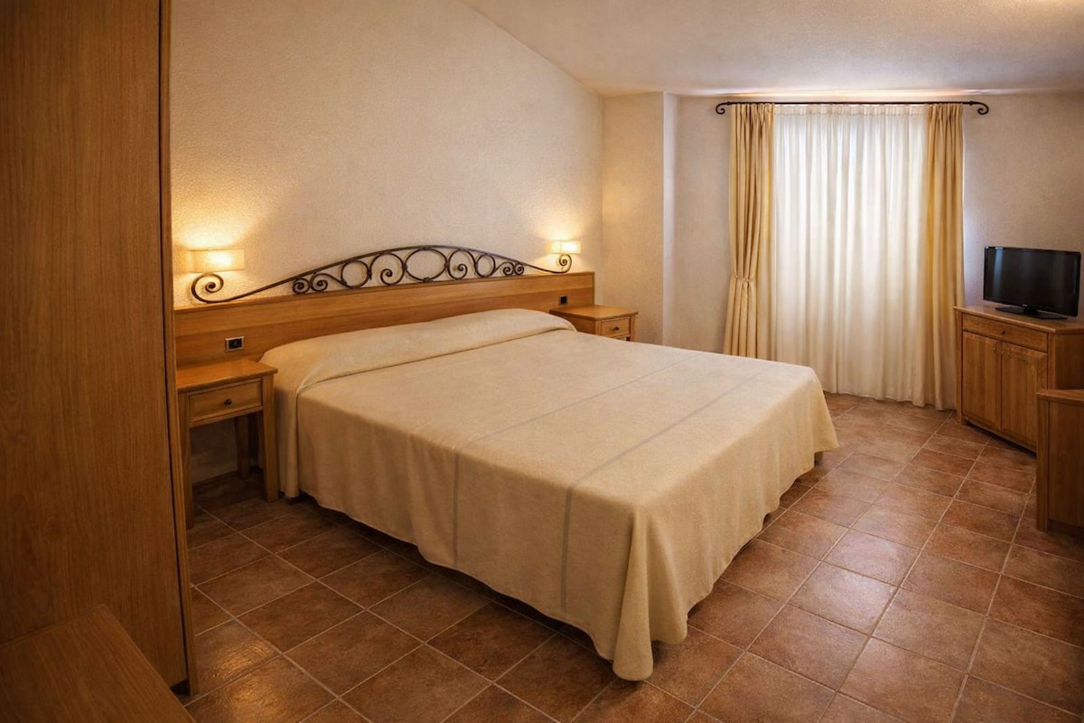 A hotel room with a bed, bedside tables, a television, and curtains.