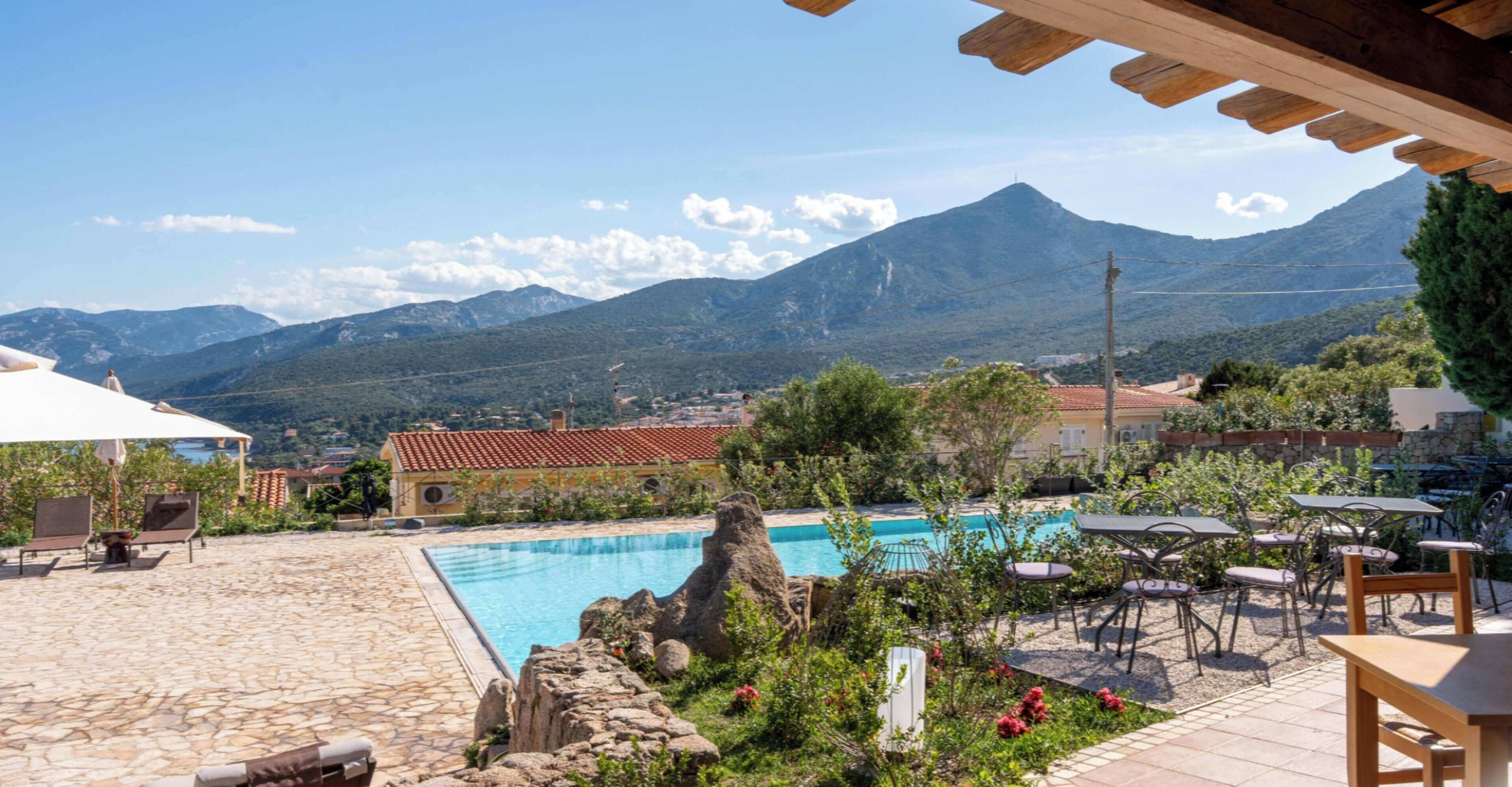A pool area with a mountain backdrop, outdoor seating, and a stone patio.
