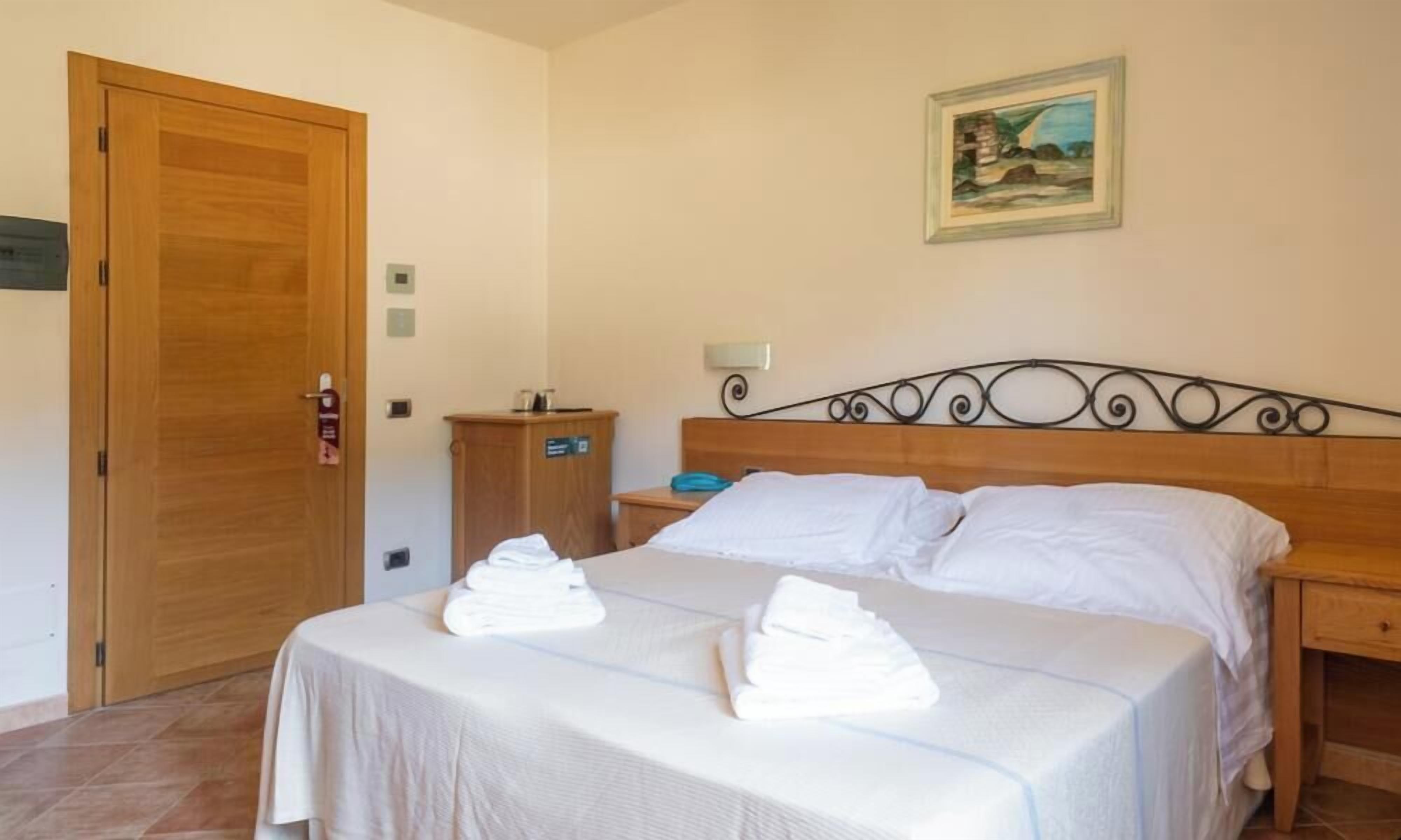 A hotel room with a wooden bed, a nightstand, a wooden wardrobe, and a painting on the wall.