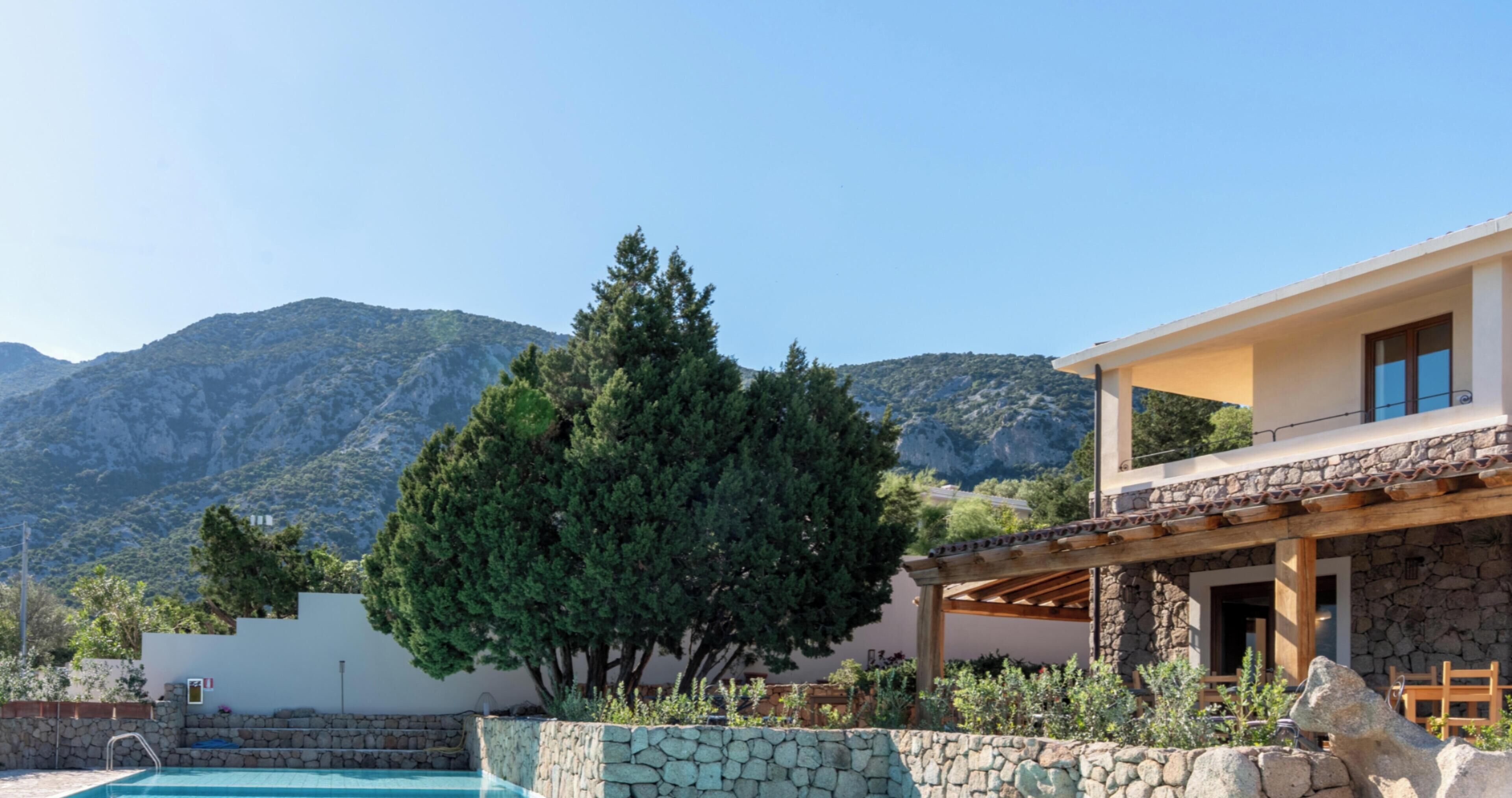 Ein Pool mit einer Steinmauer, einer Holzpergola und einem Berg im Hintergrund.