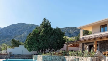 Ein Pool mit einer Steinmauer, einer Holzpergola und einem Berg im Hintergrund.