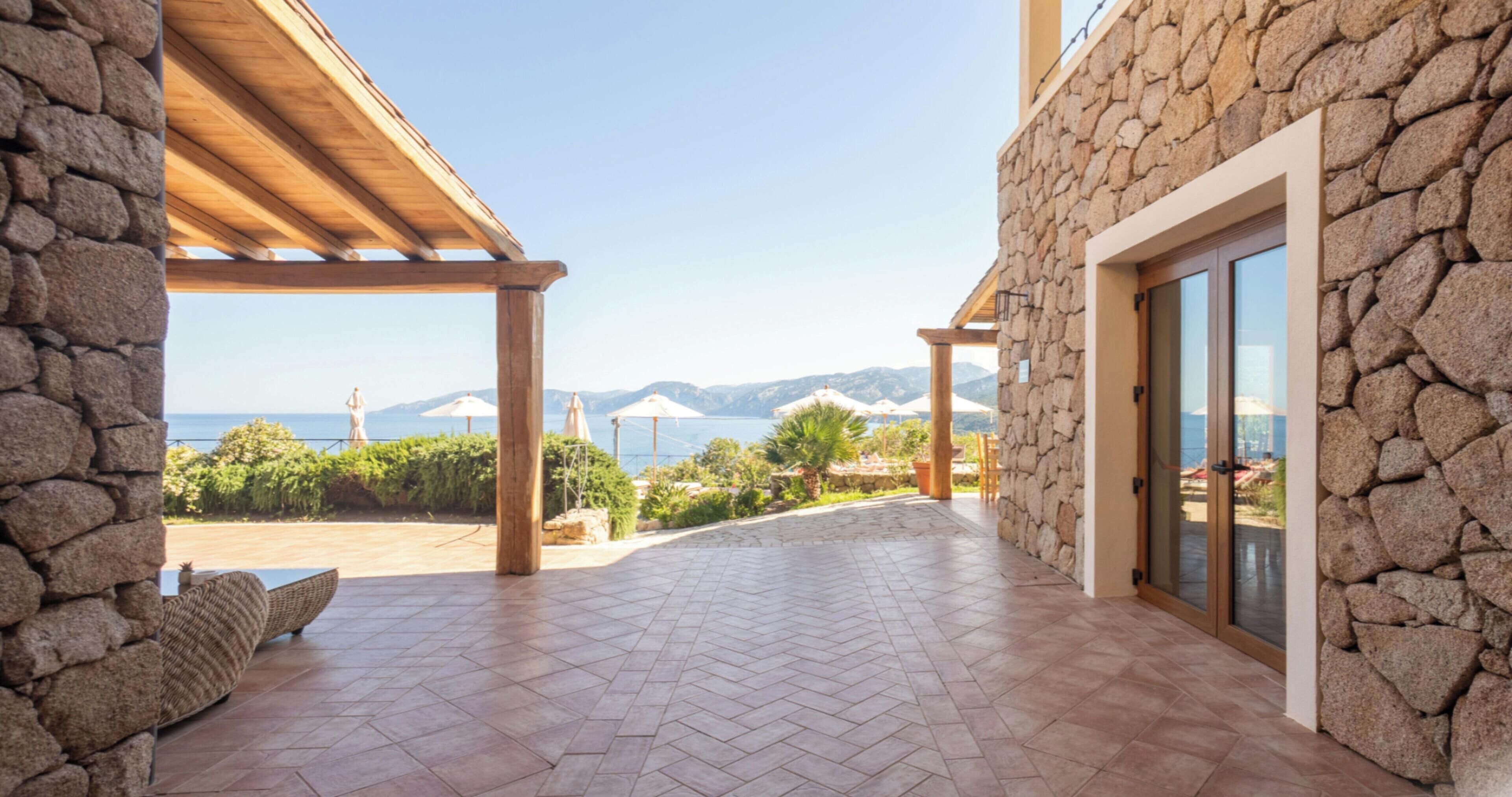 Un bâtiment en pierre doté d’un patio couvert, offrant une vue sur la mer et un paysage montagneux.