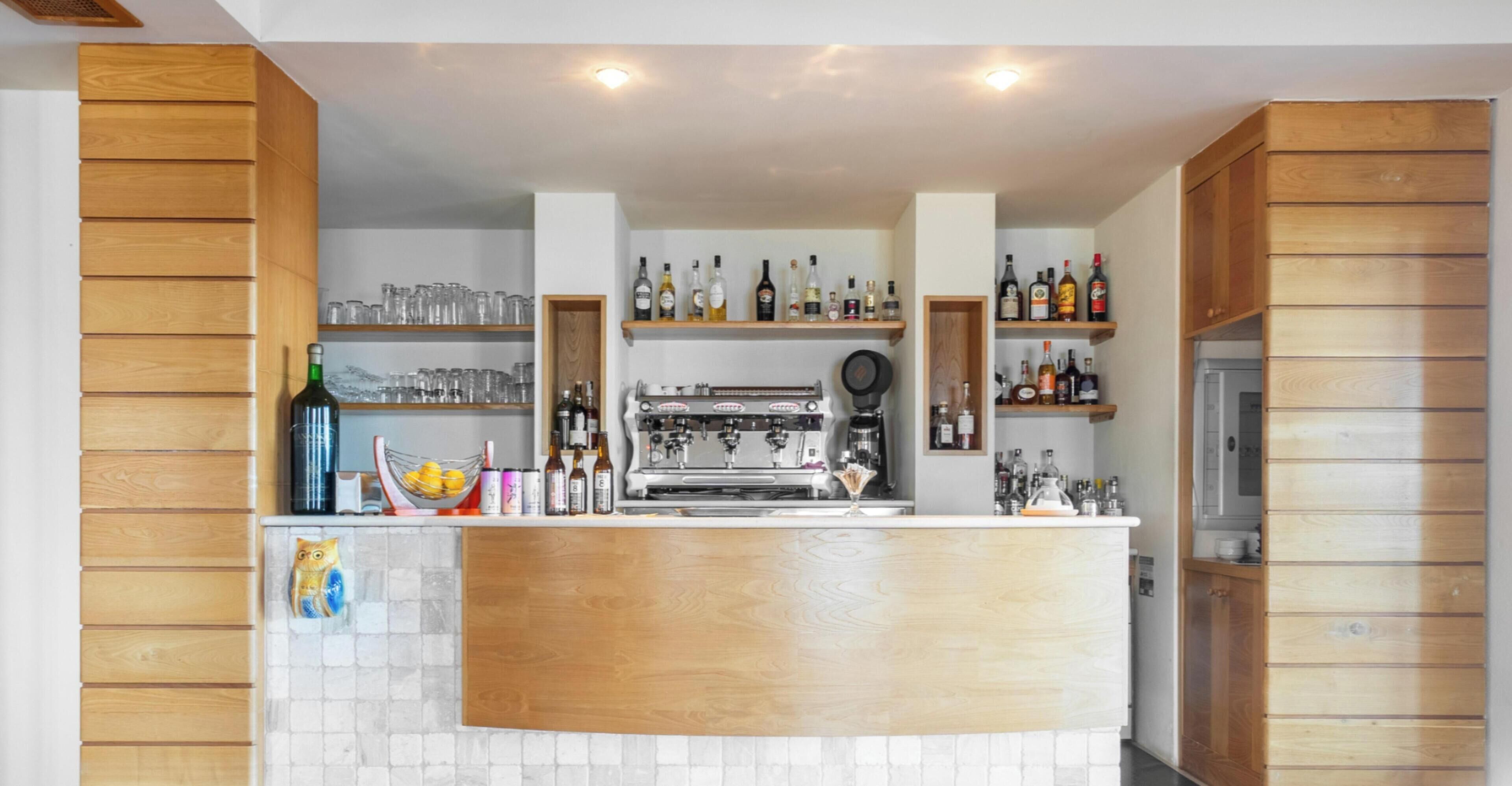 Una zona de bar con paneles de madera, estantes con botellas, vasos y una cafetera.