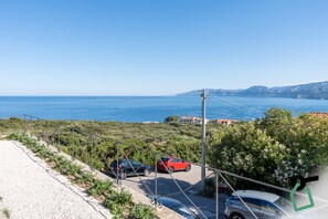 A coastal road with parked cars, a clear sky, and a view of the sea and distant mountains. - Hotiday Cala Gonone (Cala Gonone)
