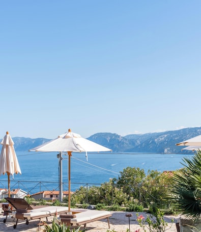 Vista sulla costa con area relax con lettini e ombrelloni, con vista sul mare e sulle montagne.. Hotiday Cala Gonone
