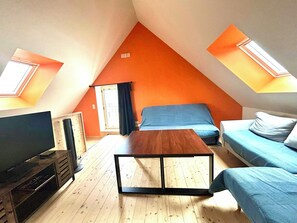 Une petite pièce triangulaire comprenant un lit, un téléviseur et une table basse en bois.