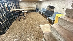 Een kamer met een betonnen vloer, bankjes, een tafel en een stenen muur.