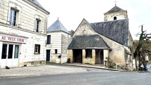 Een historisch gebouw met een kerktoren, een winkel genaamd 'Au Vieux Chene', en geplaveide straten.