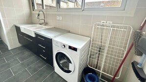 Een kleine wasruimte met een wasmachine, een wasbak en een droogrek.
