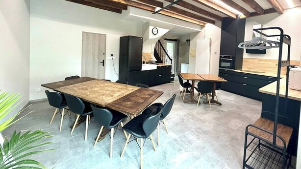 Een moderne keuken met een houten plafond, een eethoek met een grote tafel en stoelen, en een kleine zithoek met een bank.