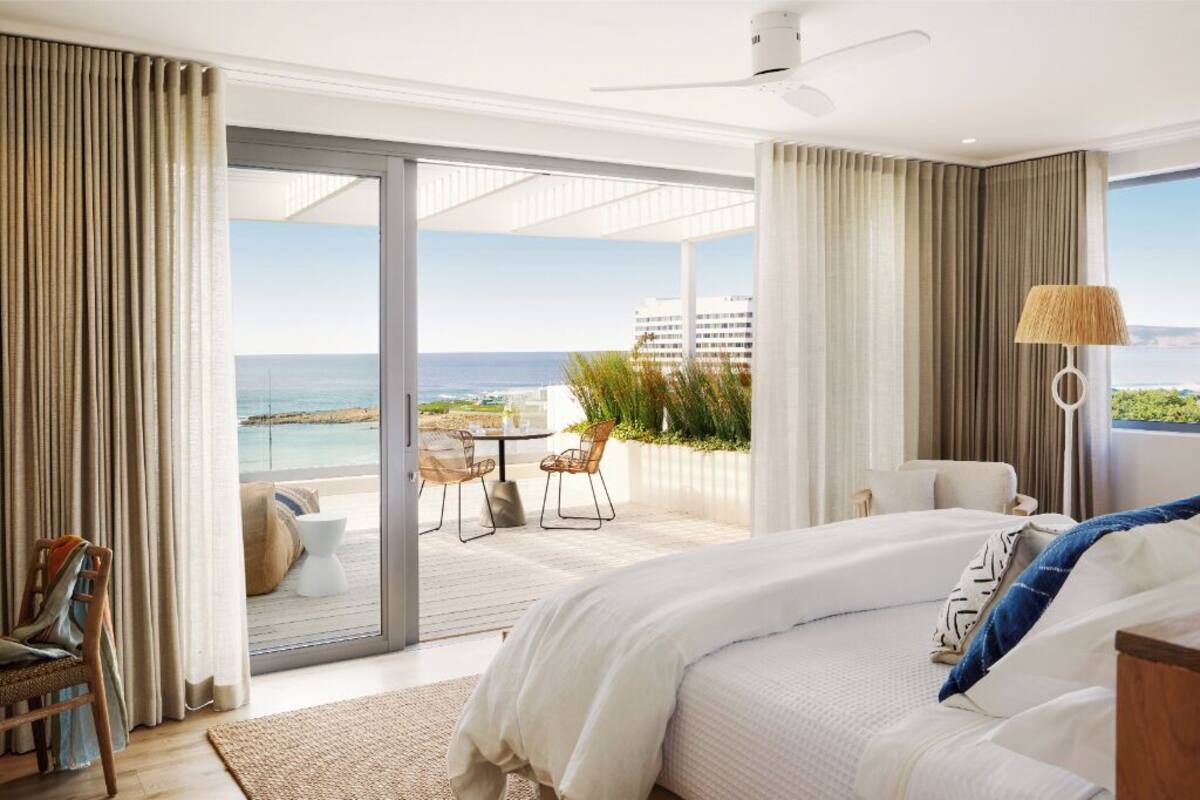 Una camera da letto con un letto, una sedia, un tavolo e vista sull'oceano.