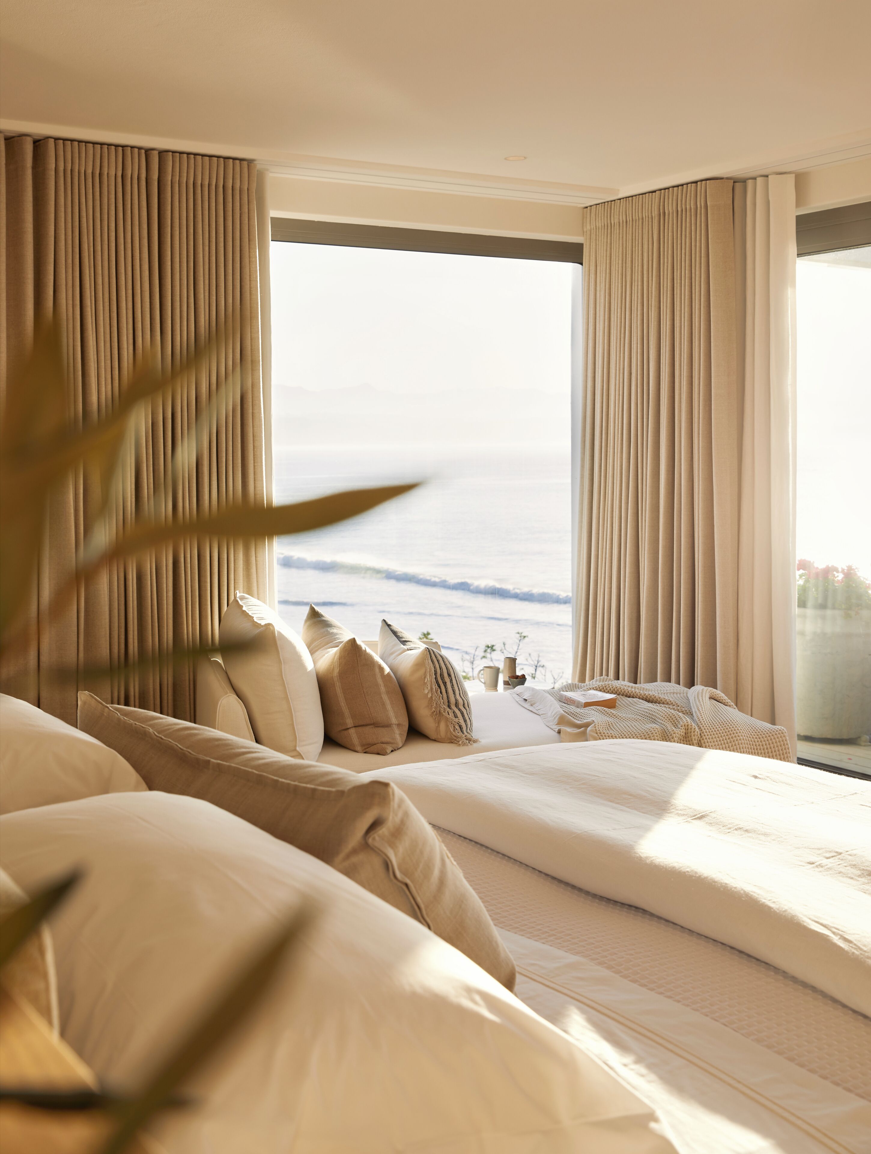 A hotel room with a large bed, a view of the sea, and a balcony with curtains.