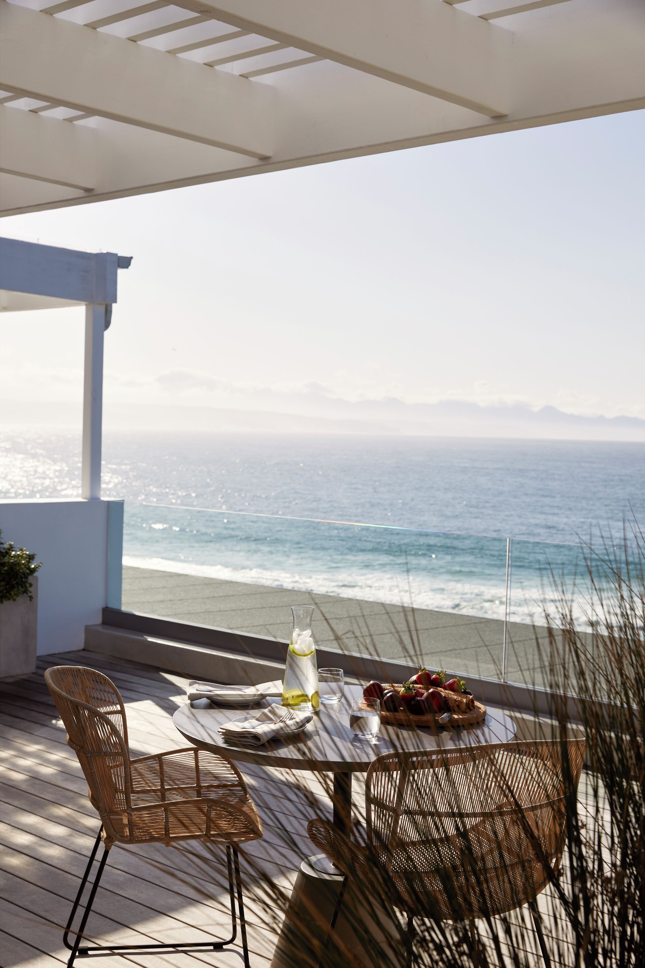 A terrace with a table and chairs, overlooking the ocean.