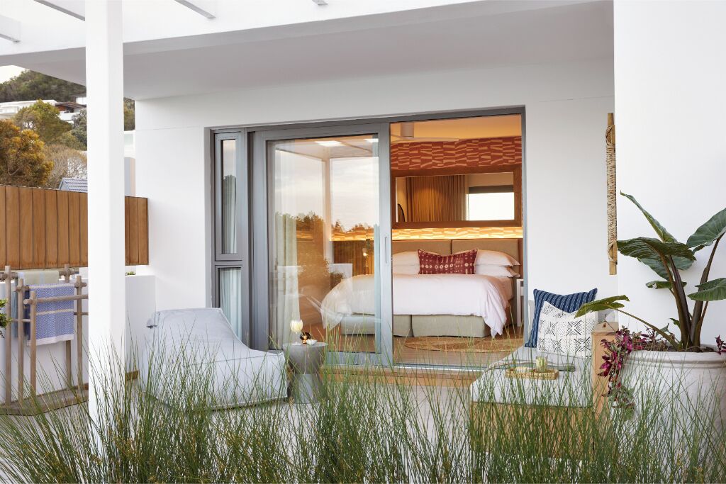 Quarto moderno com porta de vidro para uma varanda, cama com travesseiros e planta em vaso.
