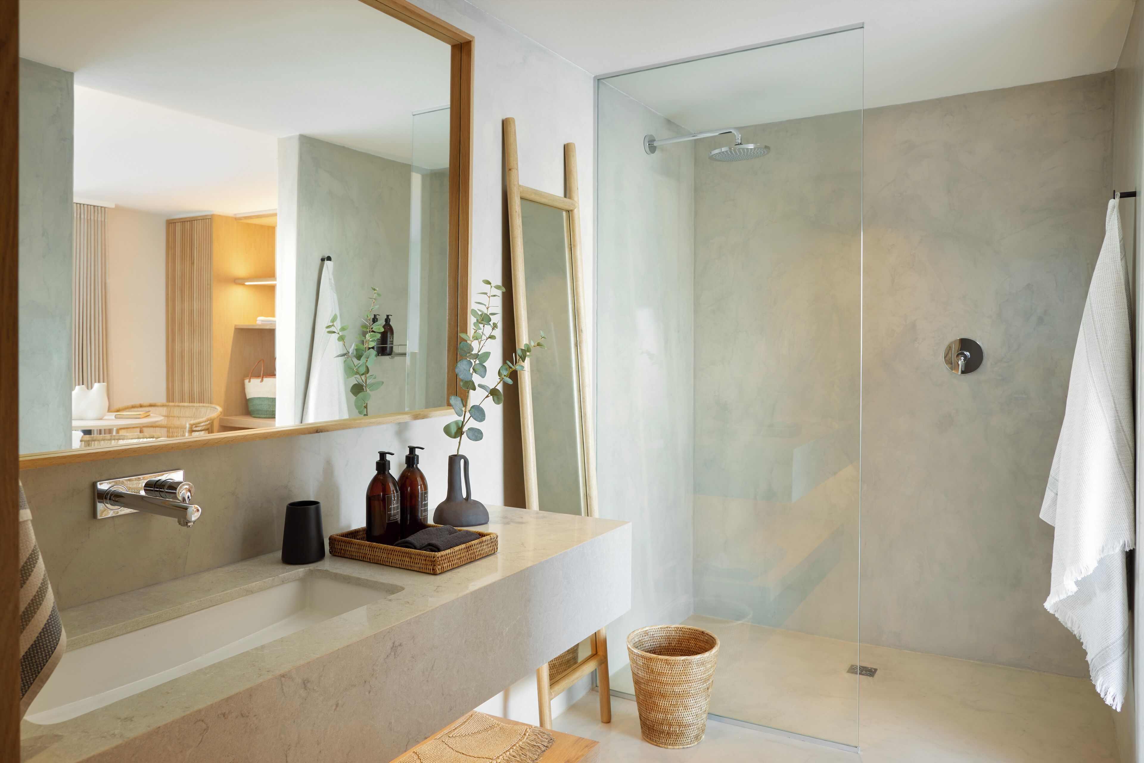 A modern bathroom with a large mirror, a glass shower enclosure, a marble countertop, and a wicker basket.