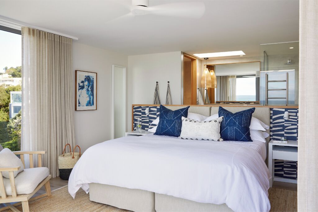 Habitación de hotel con cama, una silla, mesita de noche, espejo y vistas al exterior.