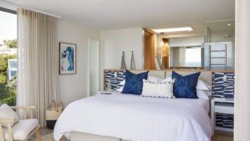 Habitación de hotel con cama, una silla, mesita de noche, espejo y vistas al exterior.