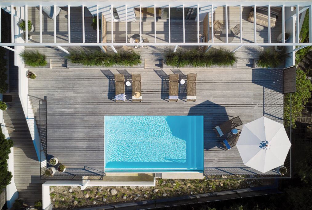An aerial view of a rooftop pool area with lounge chairs and an umbrella.