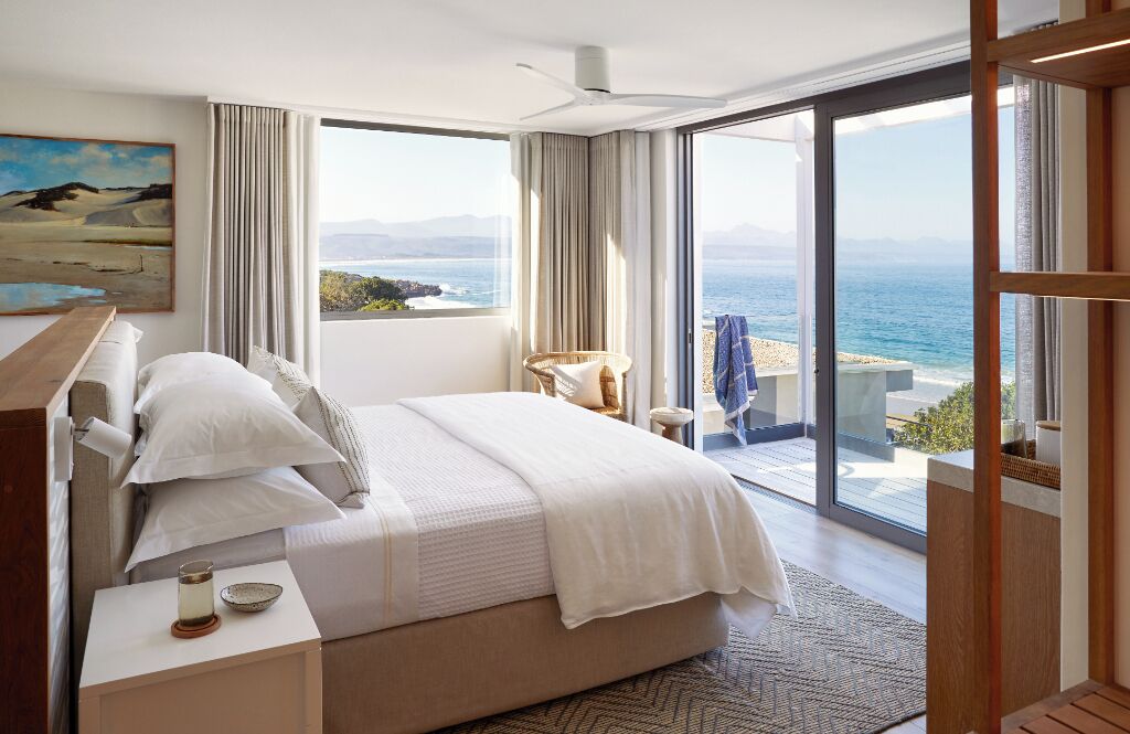 Een slaapkamer met een groot bed, uitzicht op zee en een balkon met een stoel.