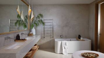 A modern bathroom with a large bathtub, two sinks, a mirror, and a plant.