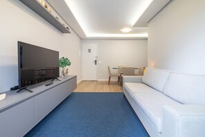 Uma sala de estar moderna com uma televisão de tela plana, um sofá, uma mesa de jantar com cadeiras e uma pequena planta.