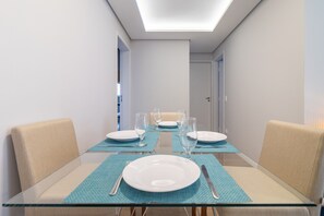 Un espace de salle à manger moderne avec des tables en verre et des chaises de couleur beige, un luminaire au plafond et une porte visible au fond.